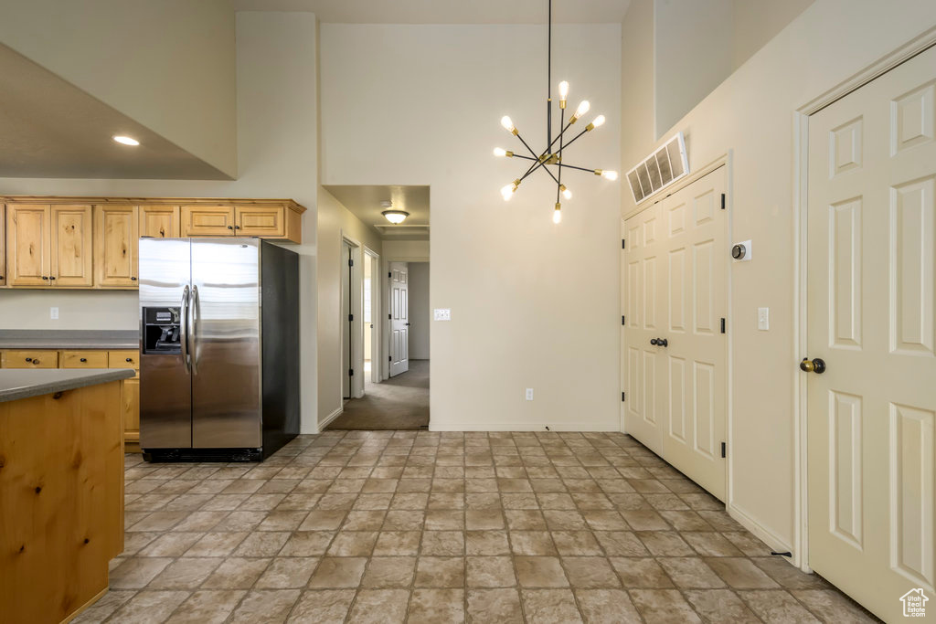 Kitchen with stone finish flooring, a chandelier, a towering ceiling, and stainless steel refrigerator with ice dispenser