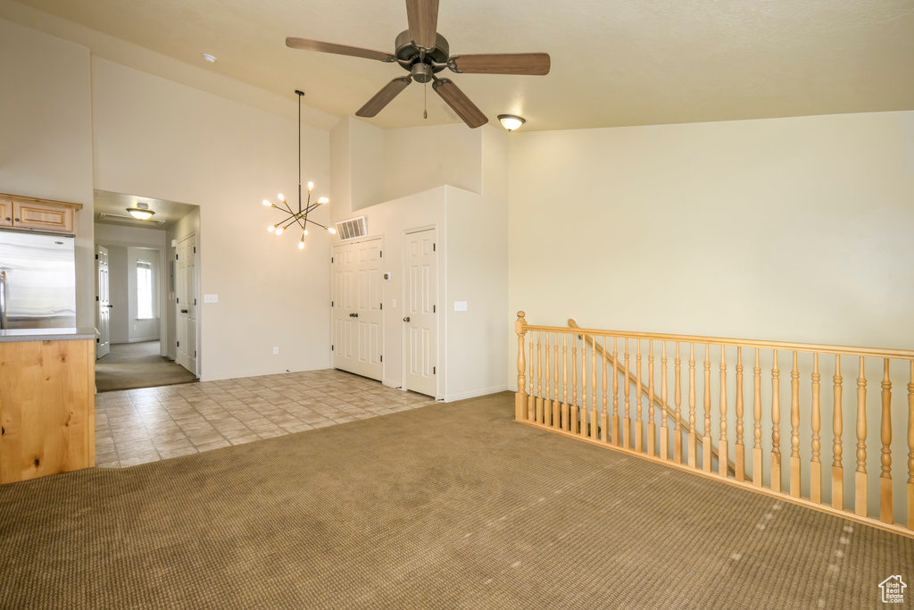 Carpeted spare room featuring visible vents, baseboards, ceiling fan with notable chandelier, and high vaulted ceiling