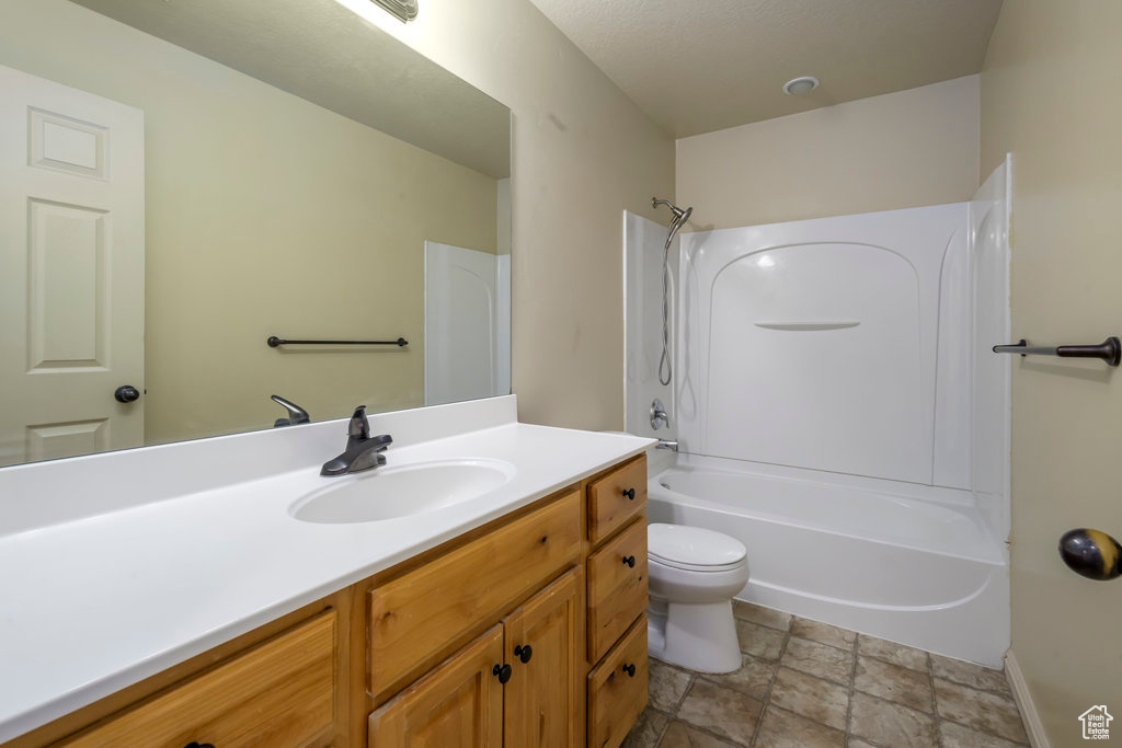 Bathroom with shower / bathtub combination, toilet, baseboards, stone finish flooring, and vanity