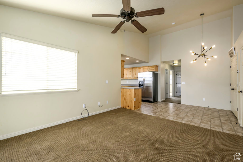 Unfurnished living room featuring baseboards, visible vents, ceiling fan with notable chandelier, high vaulted ceiling, and carpet floors