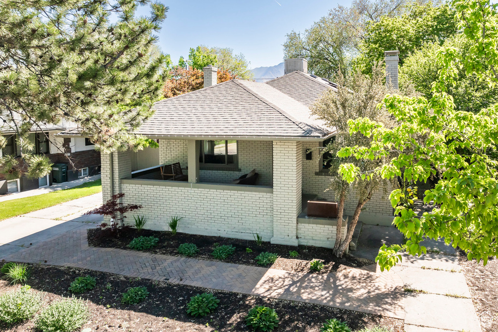 View of front of home featuring brick siding, roof with shingles, and a chimney