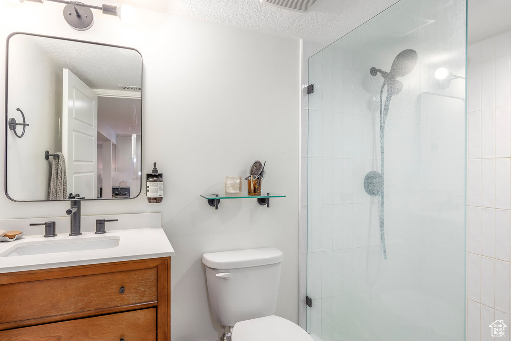 Bathroom featuring toilet, a tile shower, vanity, and a textured ceiling