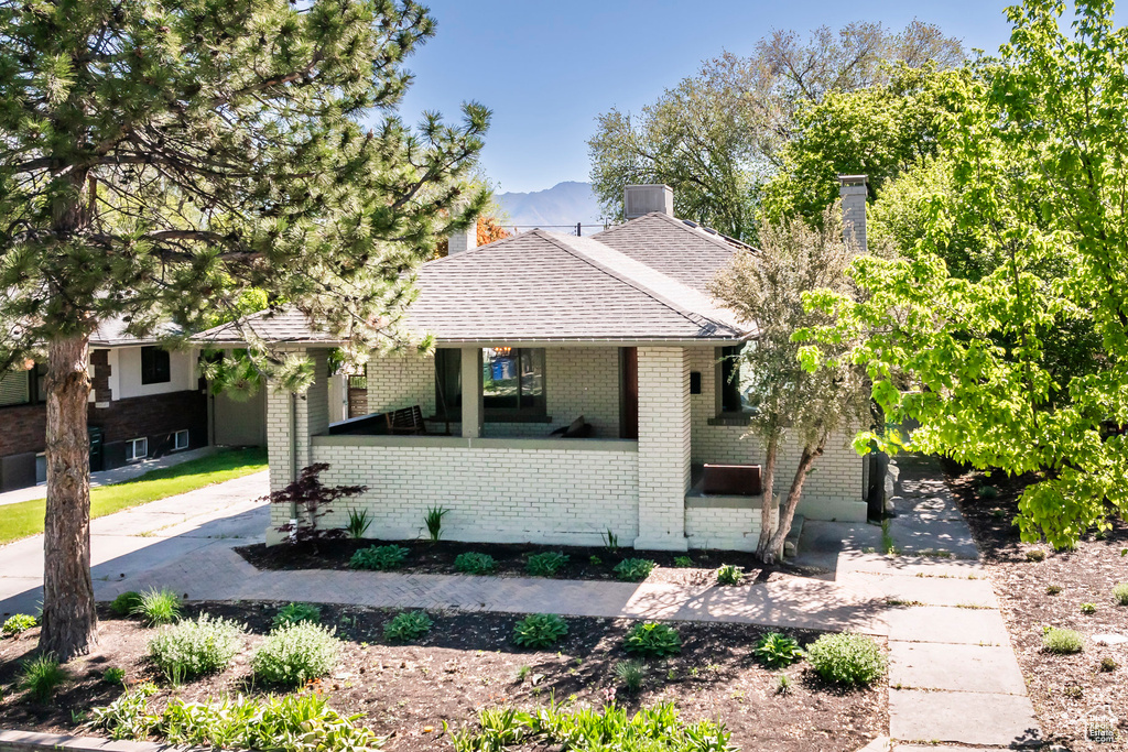 View of front of property featuring covered porch, a mountain view, a chimney, brick siding, and roof with shingles