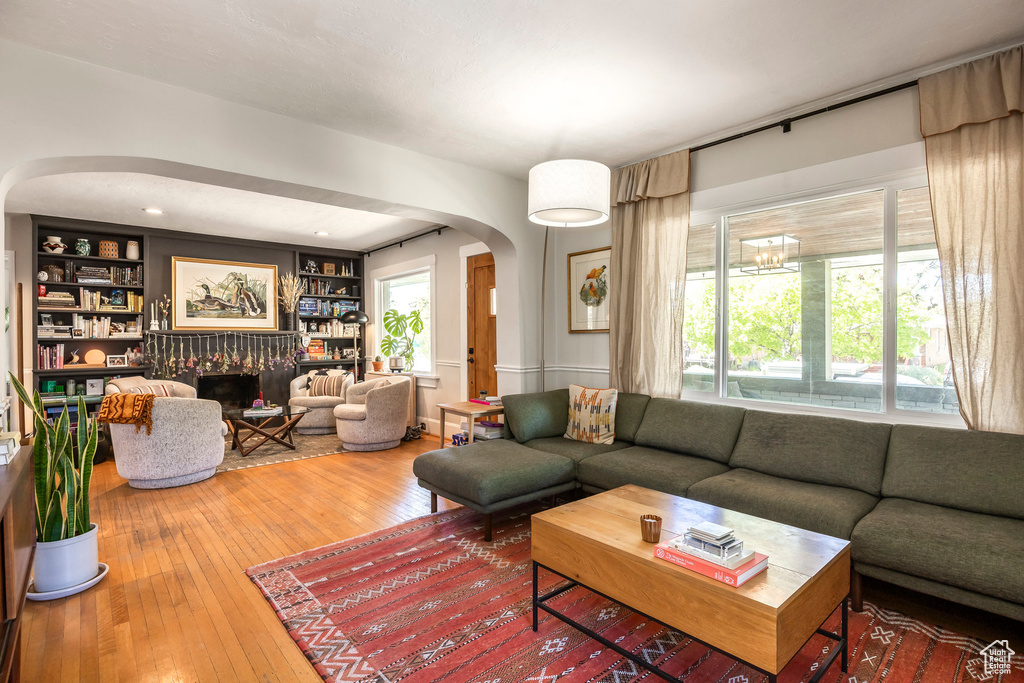 Living room featuring wood-type flooring, built in features, a fireplace, and arched walkways
