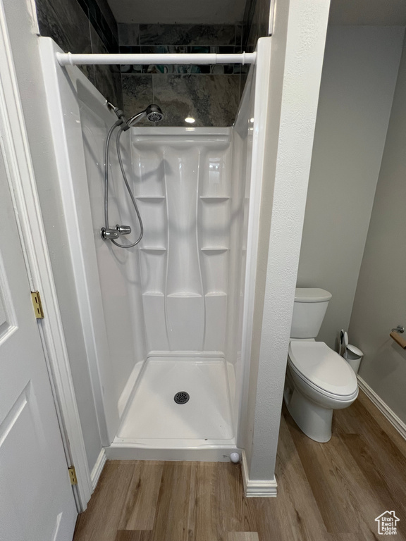 Bathroom with toilet, baseboards, a shower stall, and wood finished floors