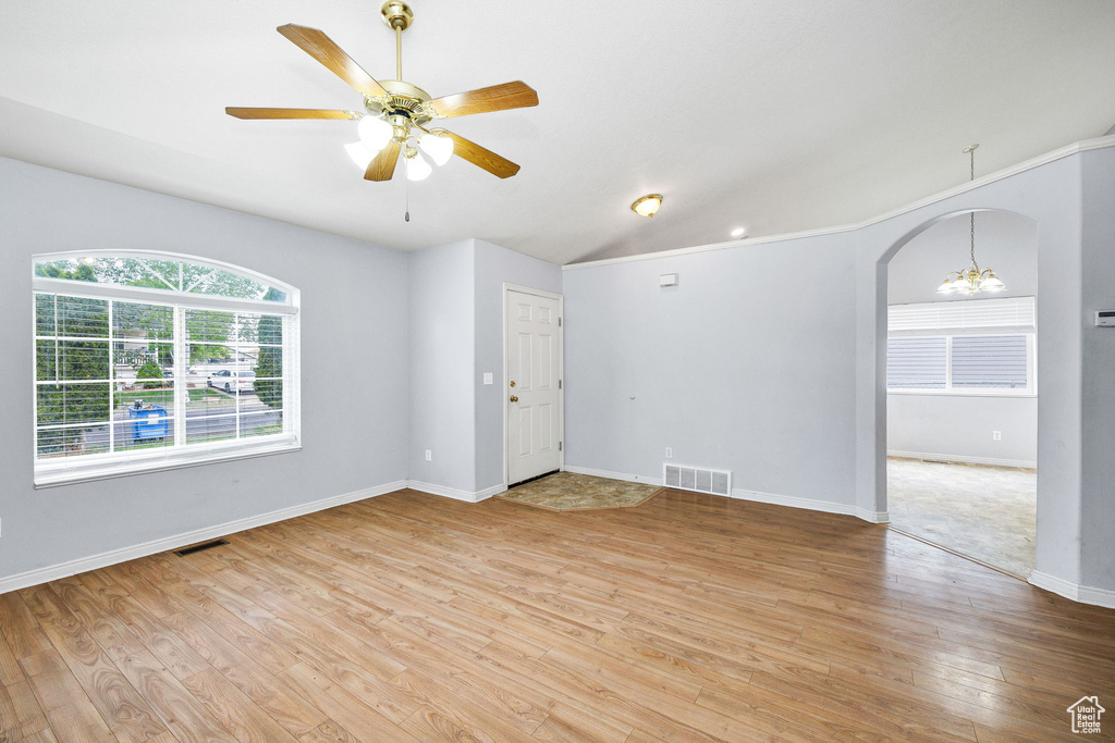 Spare room with light wood finished floors, vaulted ceiling, ceiling fan, arched walkways, and baseboards
