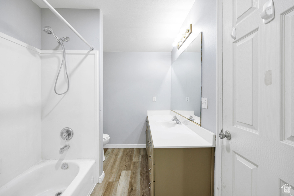 Full bath featuring vanity, toilet, wood finished floors, washtub / shower combination, and baseboards