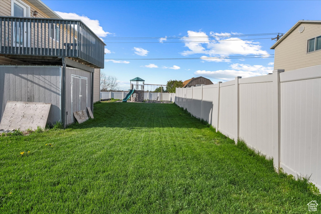 View of yard with a deck, a fenced backyard, a shed, a playground, and an outbuilding