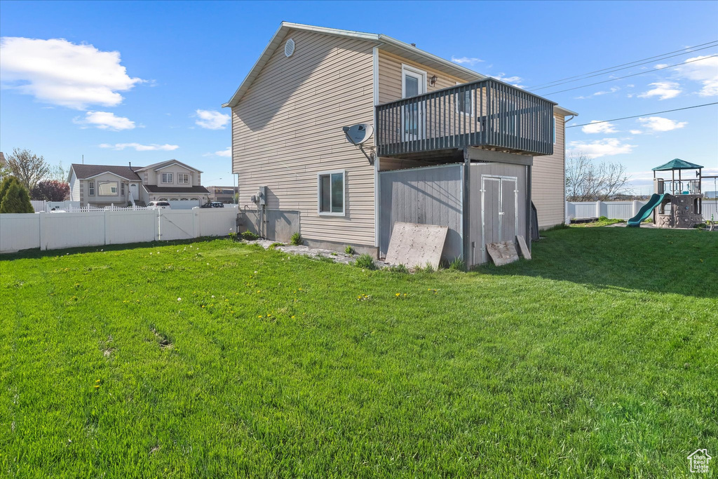 Back of house featuring a yard, fence, a wooden deck, and a playground
