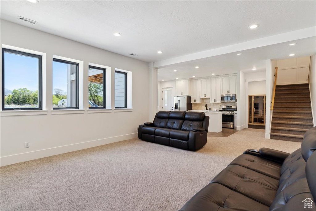 Living room with light colored carpet, visible vents, recessed lighting, stairway, and baseboards
