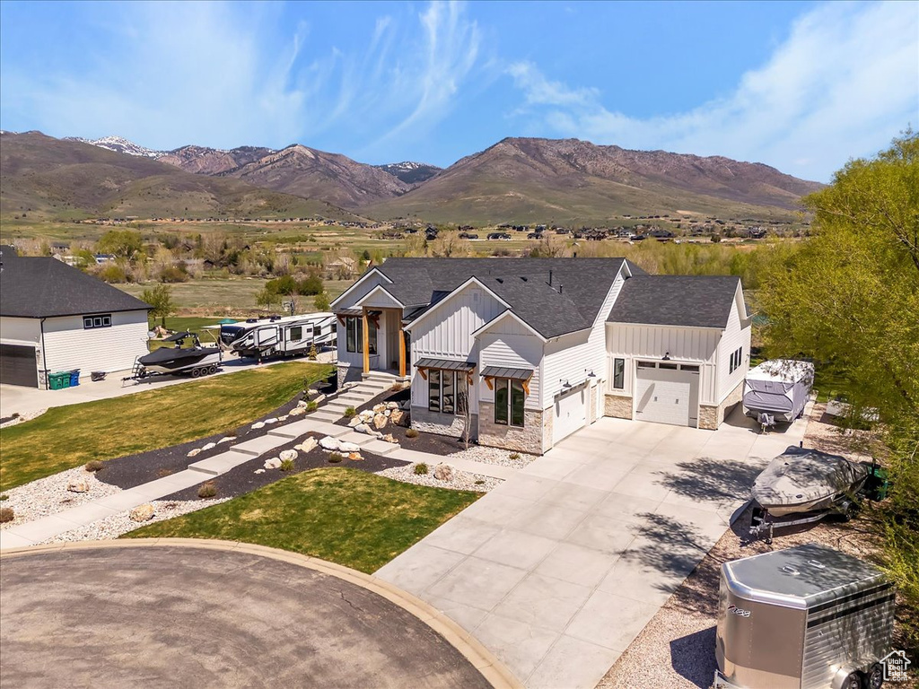 View of front of property featuring a mountain view, driveway, stone siding, a front lawn, and board and batten siding