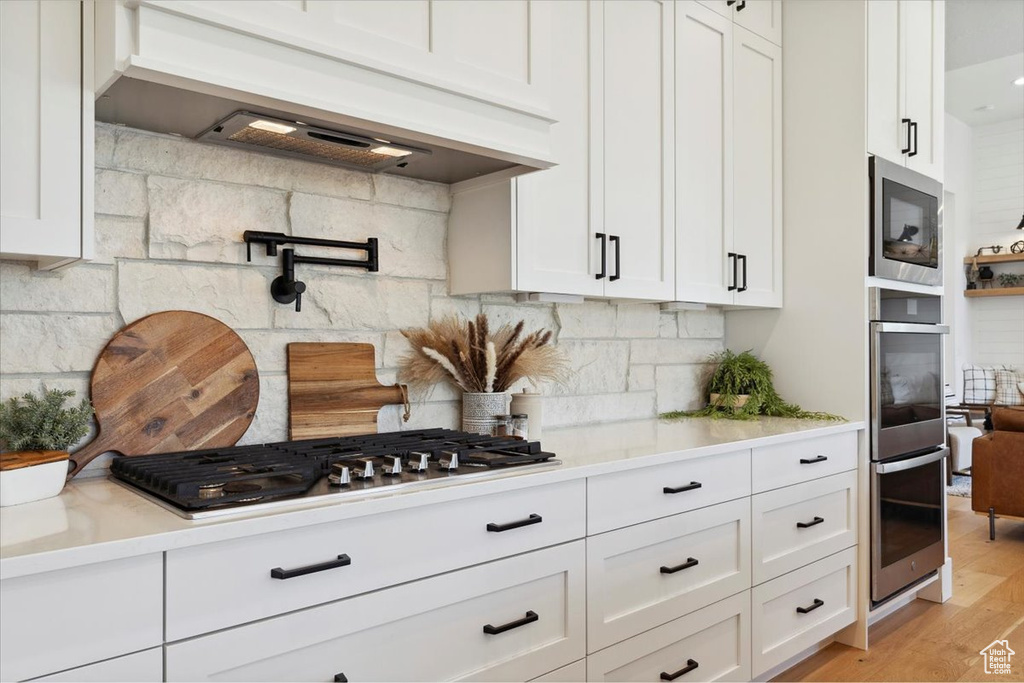 Kitchen featuring appliances with stainless steel finishes, custom range hood, and white cabinetry