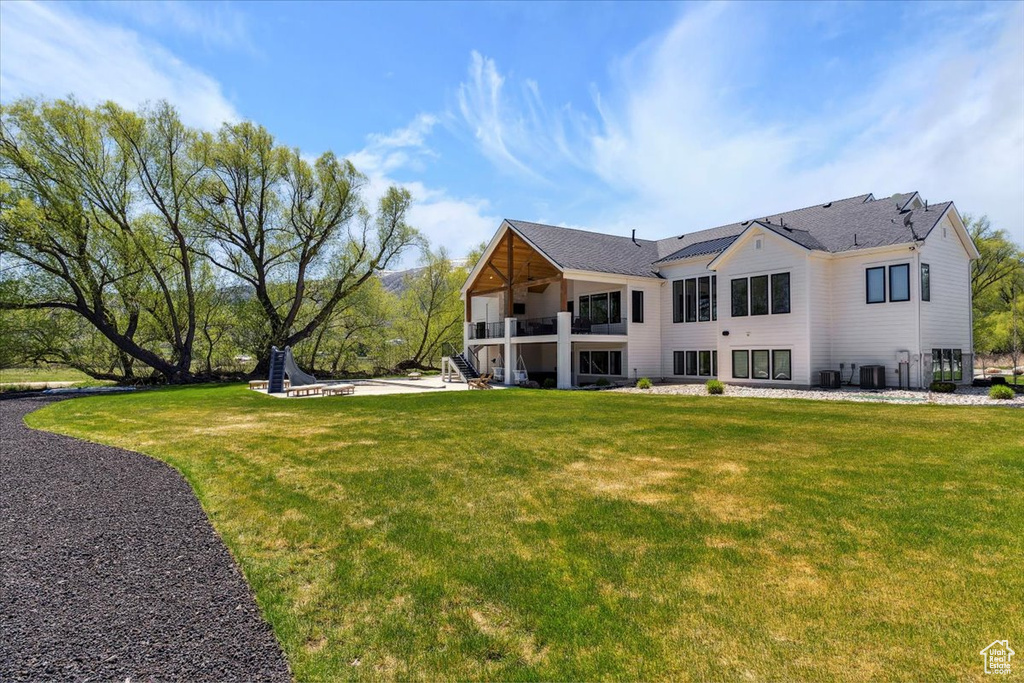 Back of property featuring central air condition unit, a lawn, and a balcony