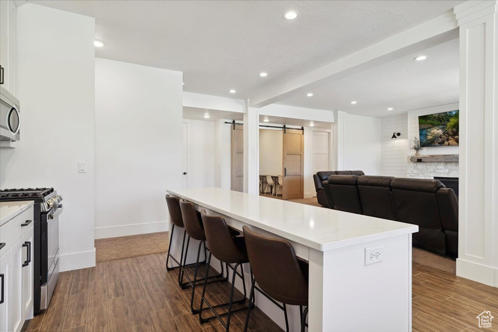 Kitchen featuring stainless steel microwave, wood finished floors, a breakfast bar, a barn door, and range with gas cooktop