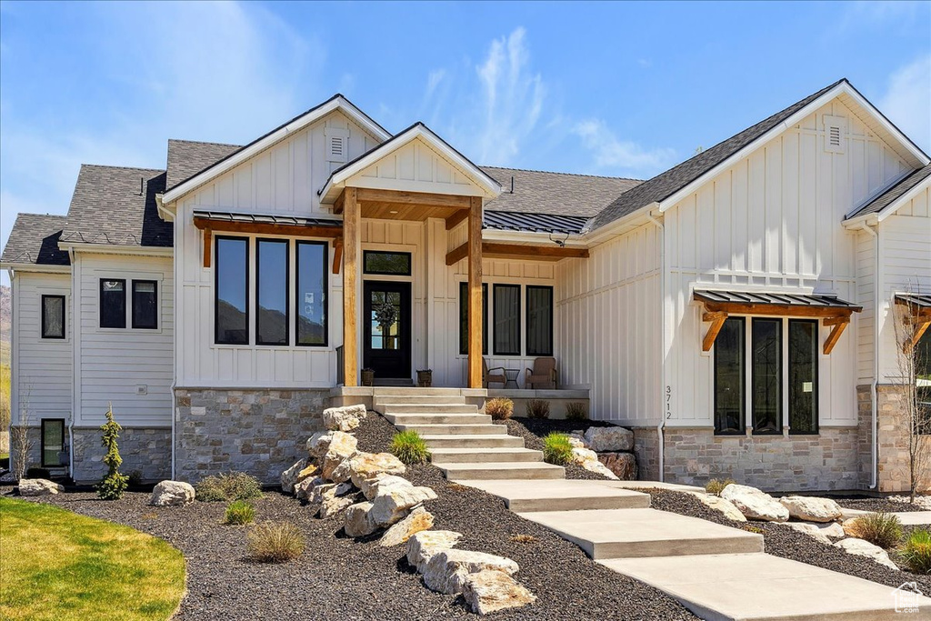 View of front of home with board and batten siding, roof with shingles, and stone siding