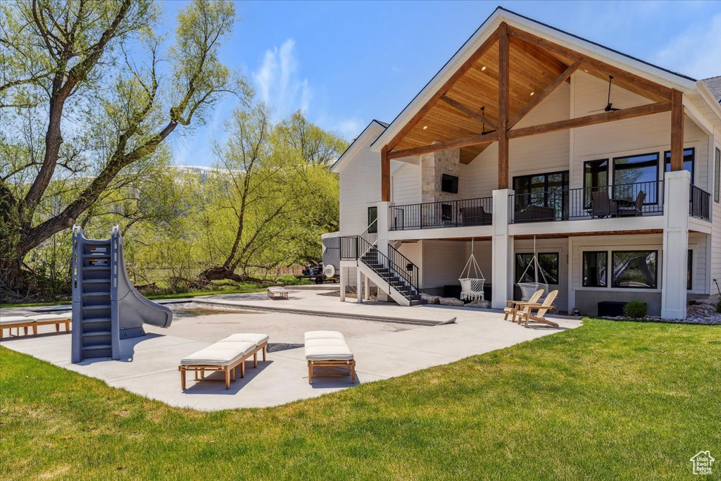 Rear view of property featuring stairway, a balcony, a patio, and a lawn