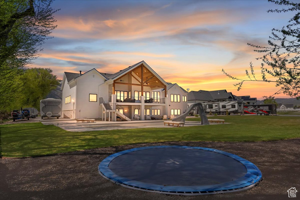 Back of property at dusk featuring a patio area, a trampoline, a balcony, stairway, and a lawn