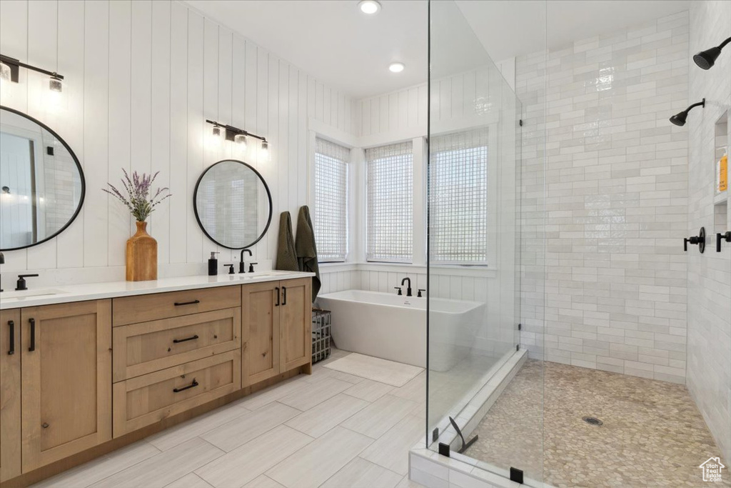 Bathroom featuring a stall shower, a soaking tub, double vanity, and a sink