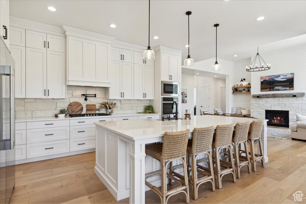 Kitchen with stainless steel microwave, a sink, white cabinetry, decorative backsplash, and light countertops