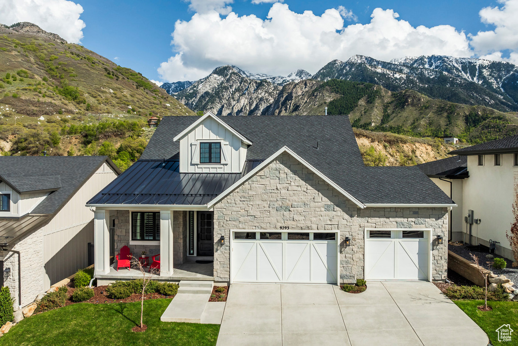 View of front of home with covered porch, a mountain view, stone siding, concrete driveway, and a standing seam roof