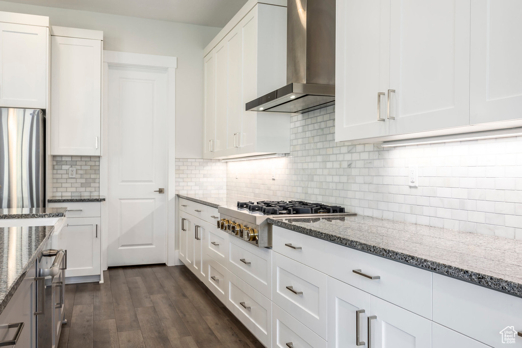 Kitchen featuring stone countertops, wall chimney exhaust hood, stainless steel appliances, and white cabinetry
