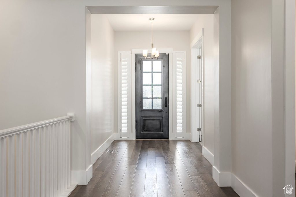 Foyer with dark wood-style flooring, a notable chandelier, and baseboards