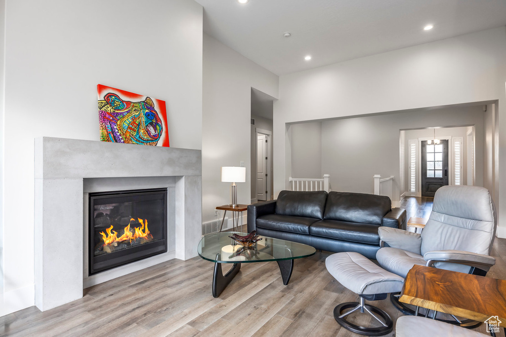 Living room with a glass covered fireplace, recessed lighting, a towering ceiling, and wood finished floors