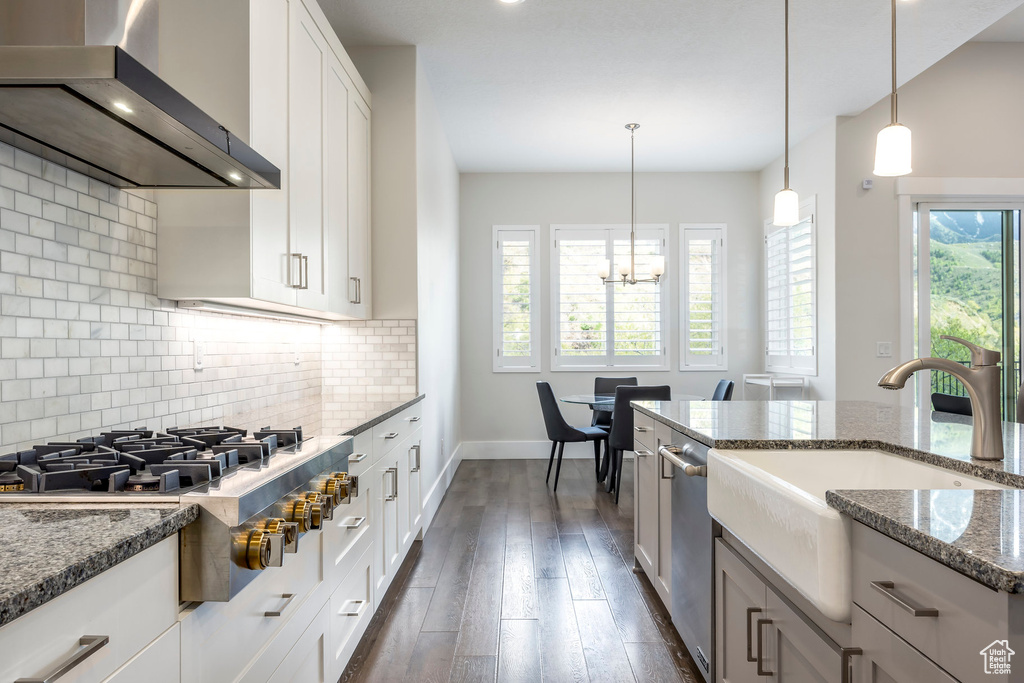 Kitchen featuring a sink, stainless steel appliances, tasteful backsplash, dark stone countertops, and wall chimney exhaust hood