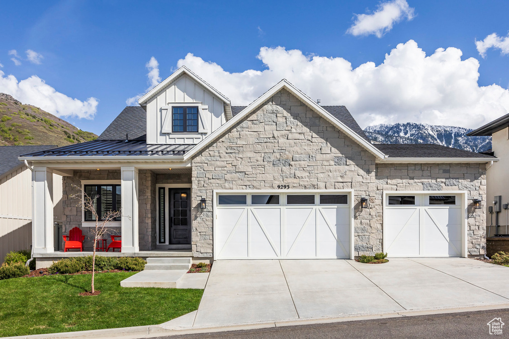 View of front of property with stone siding, an attached garage, board and batten siding, driveway, and a standing seam roof