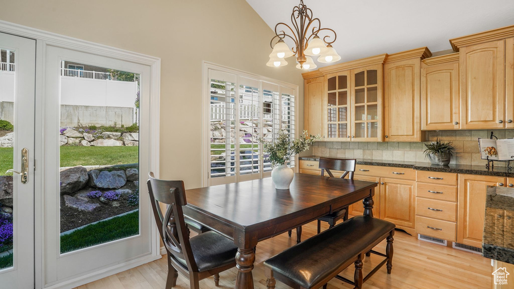 Dining room with light wood finished floors, an inviting chandelier, visible vents, and lofted ceiling