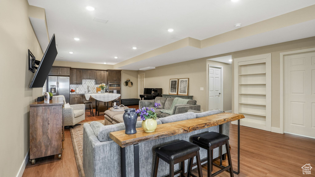 Living room with light wood finished floors, built in features, baseboards, and recessed lighting
