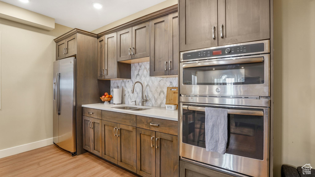 Kitchen featuring a sink, stainless steel appliances, light wood-type flooring, decorative backsplash, and baseboards