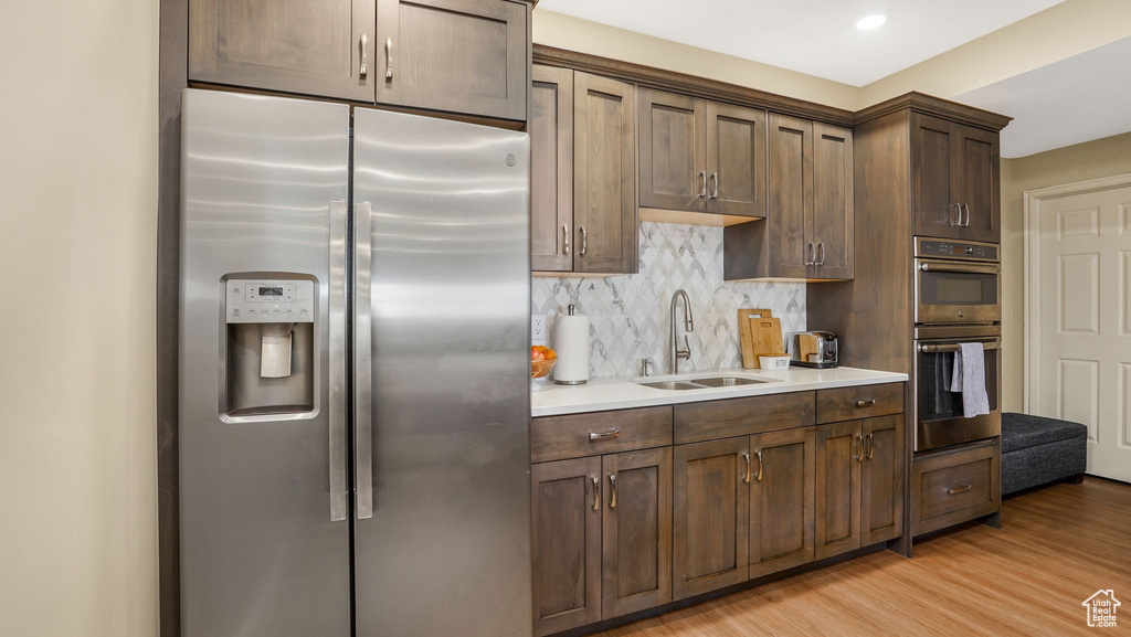 Kitchen featuring a sink, stainless steel appliances, tasteful backsplash, light countertops, and light wood-style floors