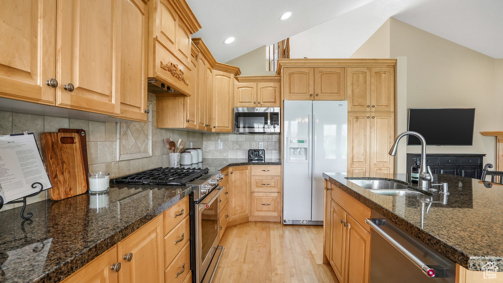 Kitchen featuring light wood finished floors, a sink, dark stone counters, stainless steel appliances, and vaulted ceiling