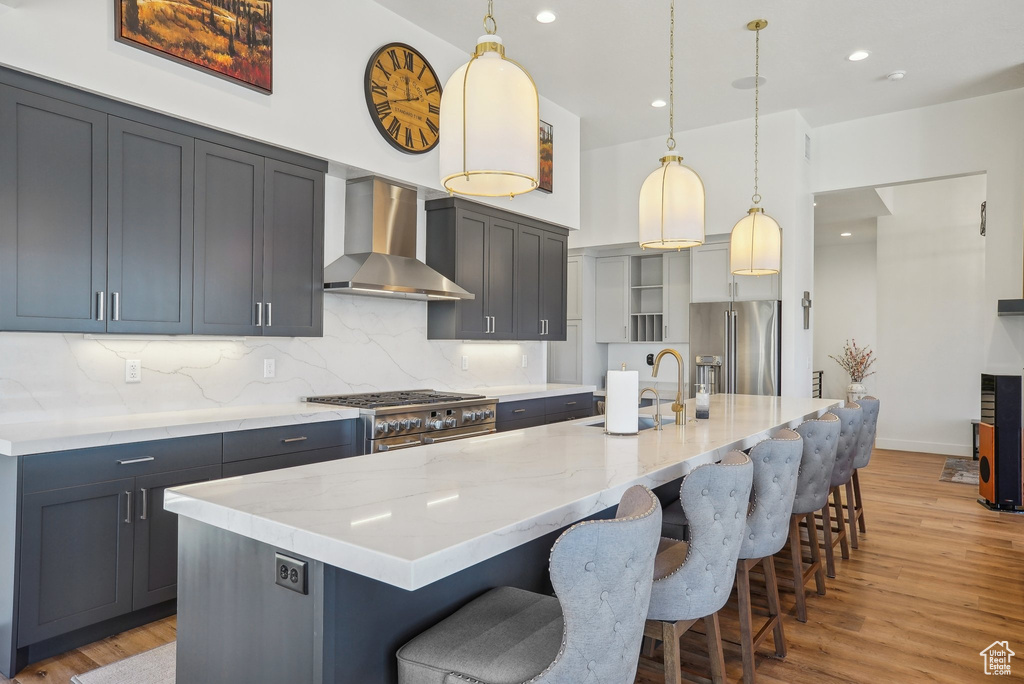 Kitchen with light wood-style flooring, a sink, wall chimney exhaust hood, high quality appliances, and light stone countertops