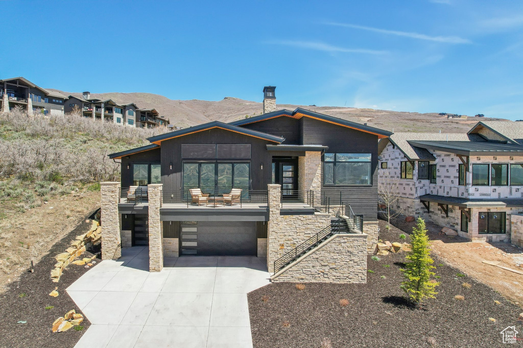 View of front of property with a chimney, driveway, a mountain view, an attached garage, and stone siding