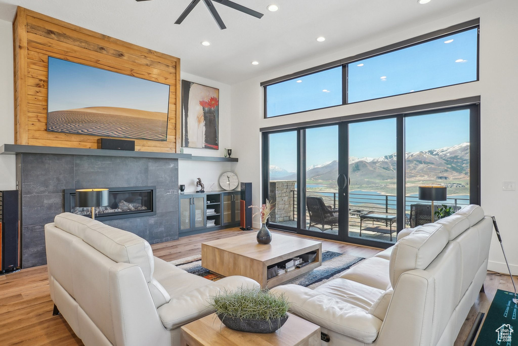 Living room featuring wood finished floors, a ceiling fan, a high ceiling, a fireplace, and recessed lighting