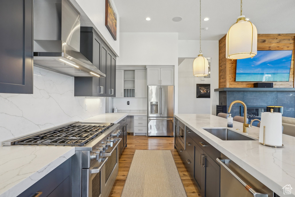 Kitchen featuring a sink, light stone counters, wall chimney exhaust hood, light wood-style flooring, and appliances with stainless steel finishes
