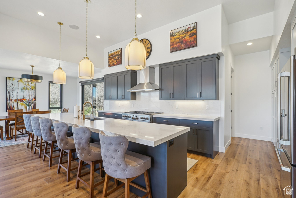 Kitchen with backsplash, wall chimney exhaust hood, a kitchen breakfast bar, and light wood-type flooring