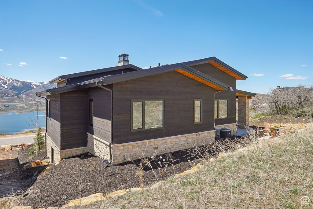 View of side of property with central AC unit, a chimney, and a water view