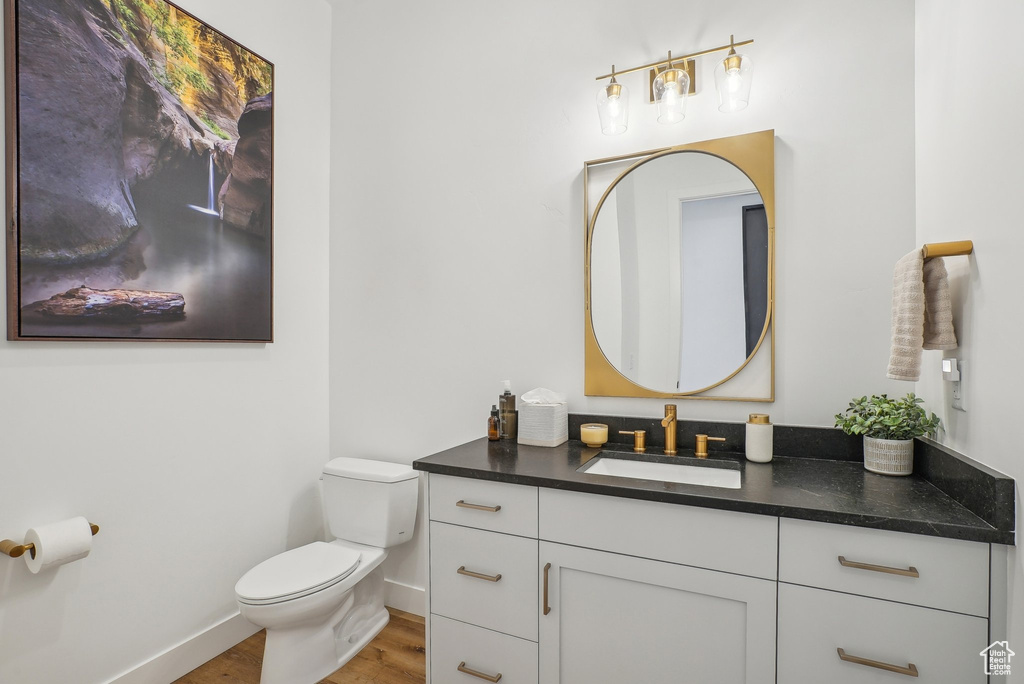 Half bath with toilet, baseboards, wood finished floors, and vanity
