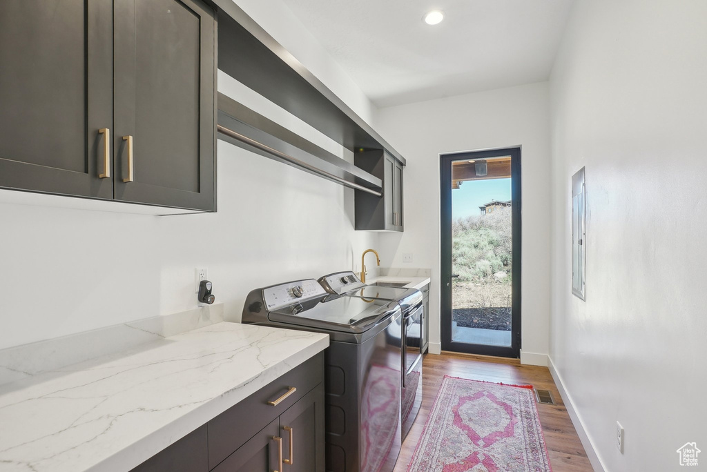 Clothes washing area with washing machine and dryer, baseboards, a sink, wood finished floors, and cabinet space