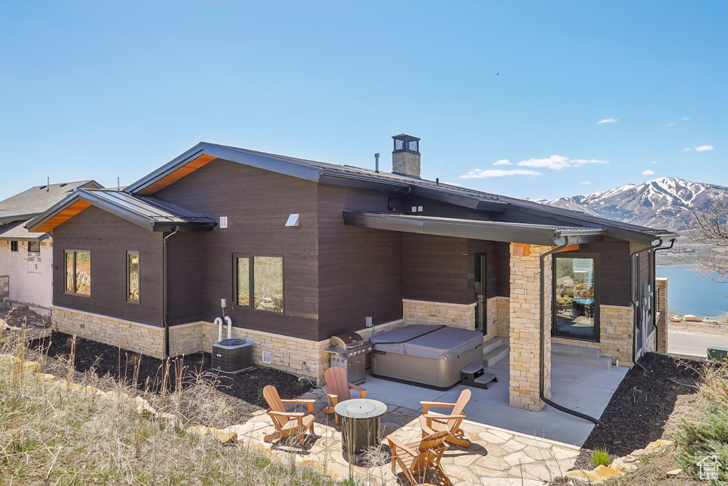 Back of property featuring stone siding, a mountain view, a hot tub, and a patio