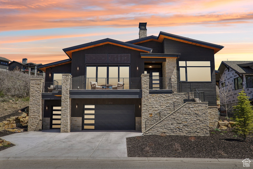 Modern home with stone siding, an attached garage, a chimney, concrete driveway, and stairway