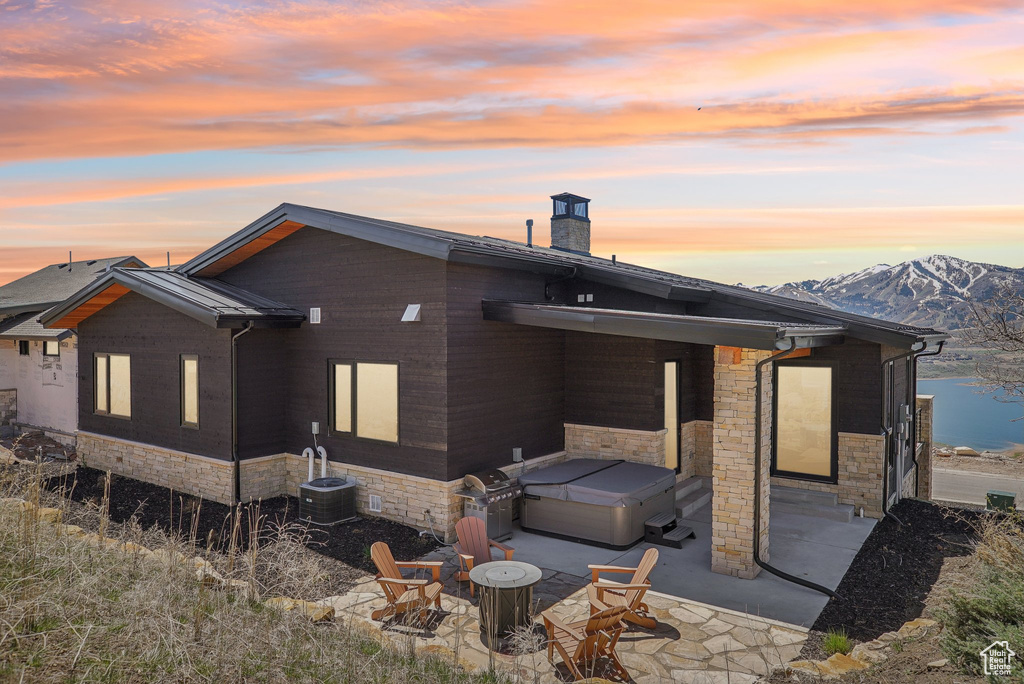Rear view of house featuring a patio area, a hot tub, stone siding, and a fire pit
