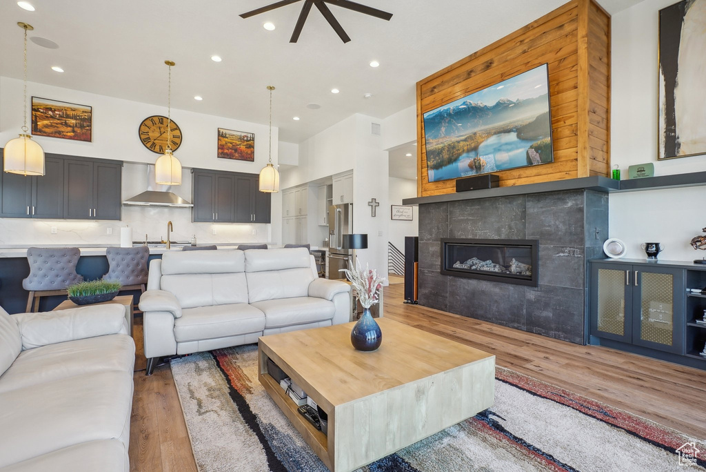 Living room with light wood-type flooring, recessed lighting, a tiled fireplace, and ceiling fan