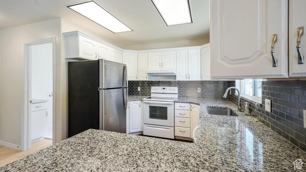Kitchen featuring white range with electric stovetop, light stone counters, a sink, freestanding refrigerator, and backsplash