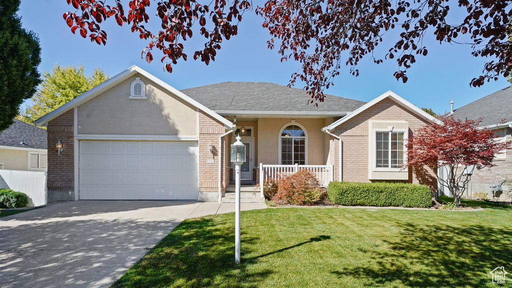 Ranch-style home featuring covered porch, driveway, a front yard, and a garage
