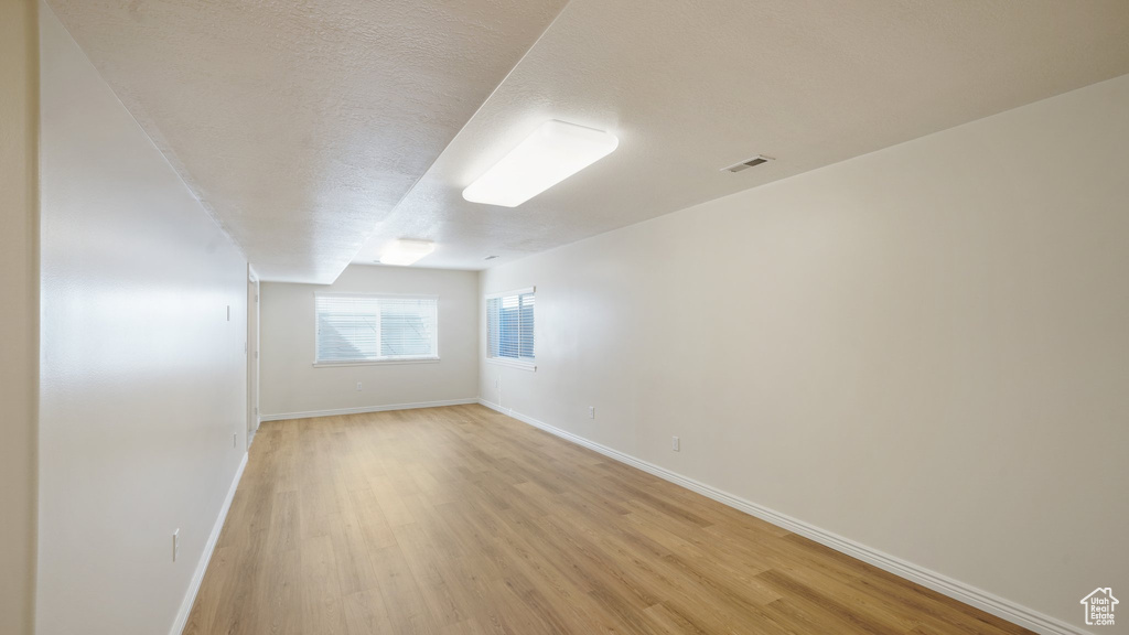 Empty room with baseboards, light wood-type flooring, a textured ceiling, and visible vents