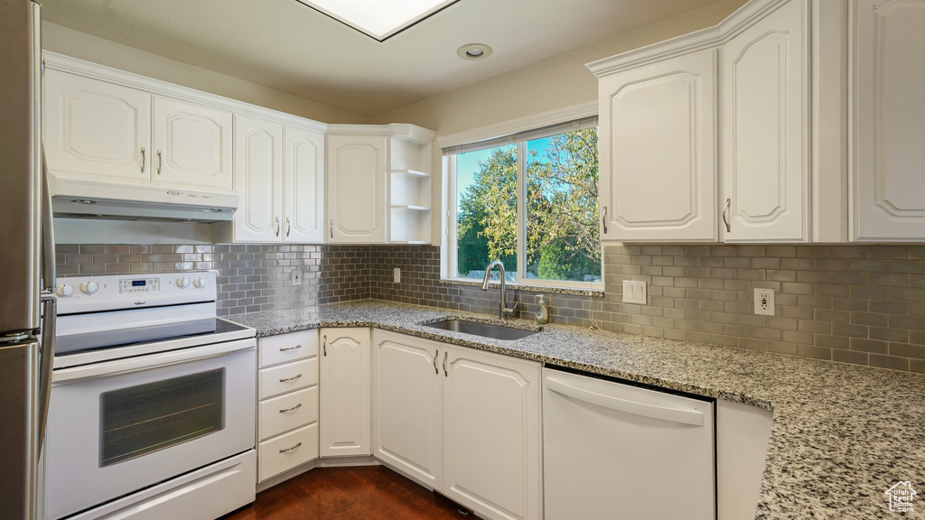 Kitchen with light stone counters, a sink, under cabinet range hood, and white appliances